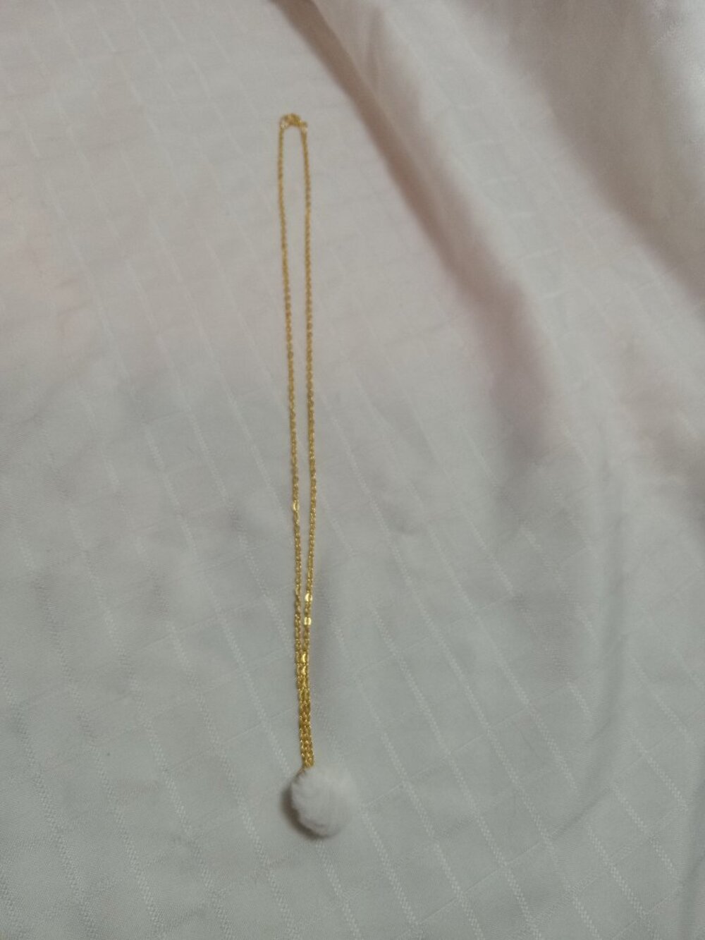 Handmade necklace with a small pom-pom and gold-colored accent hooks and chains